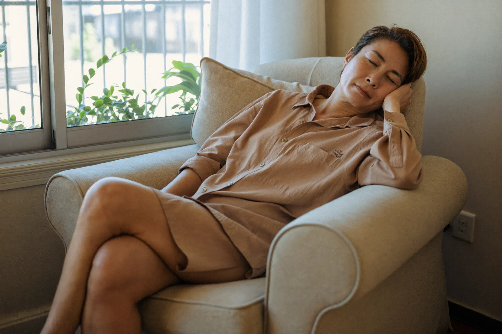 窓辺のひじ掛け椅子で昼寝をする50代の女性