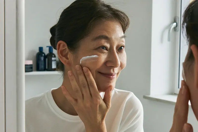 洗面所の鏡の前で、指先で頬に保湿剤をなじませる女性