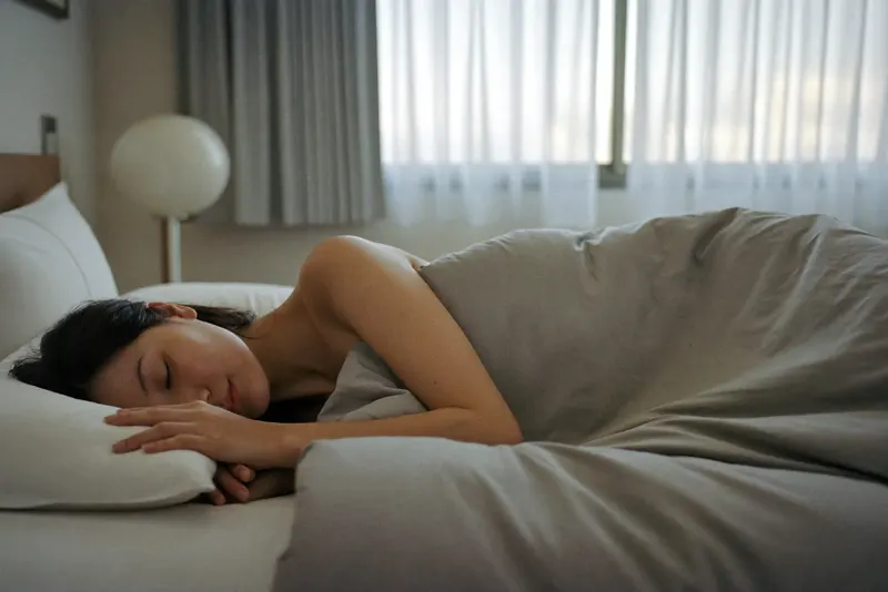 朝の光が差す寝室で、横向きに眠る女性